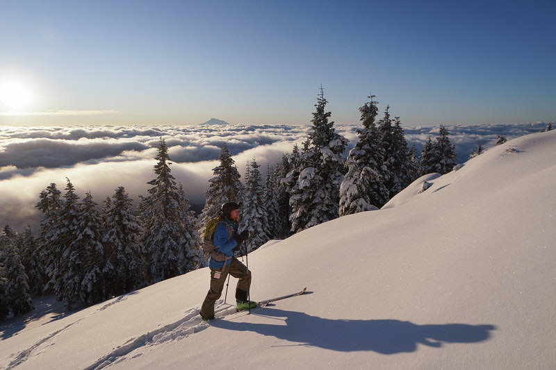 A skier climbing a snowy slope above a sea of clouds